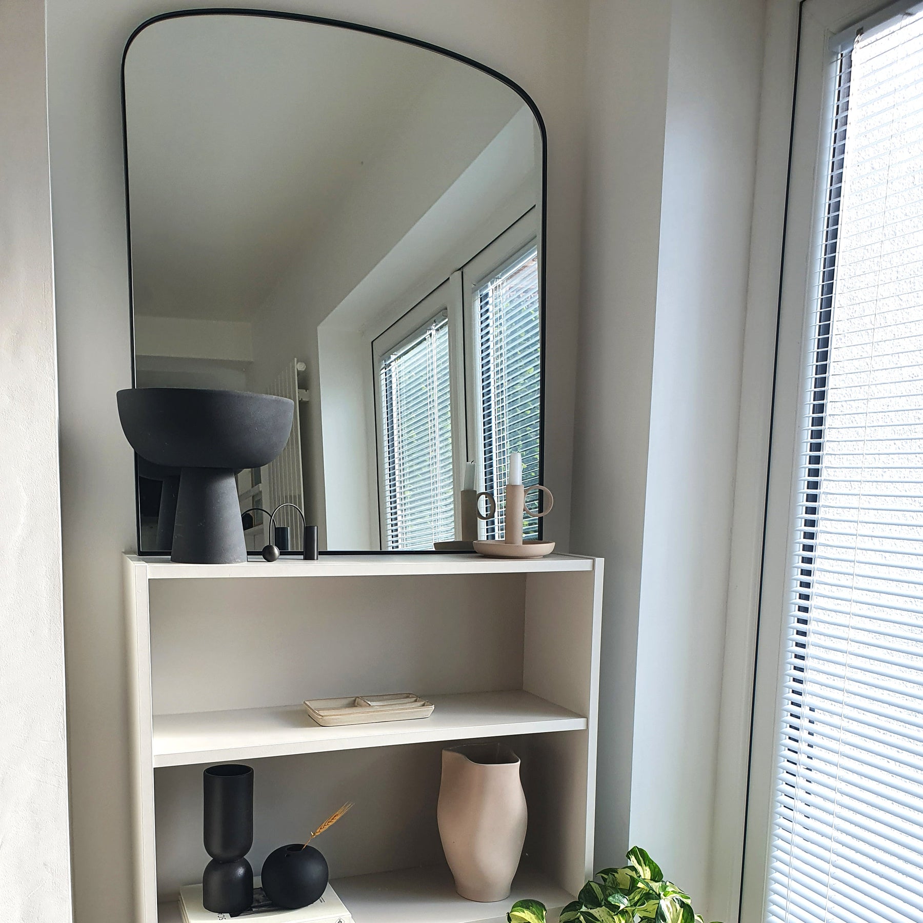 Black contemporary arched metal wall mirror displayed beside window