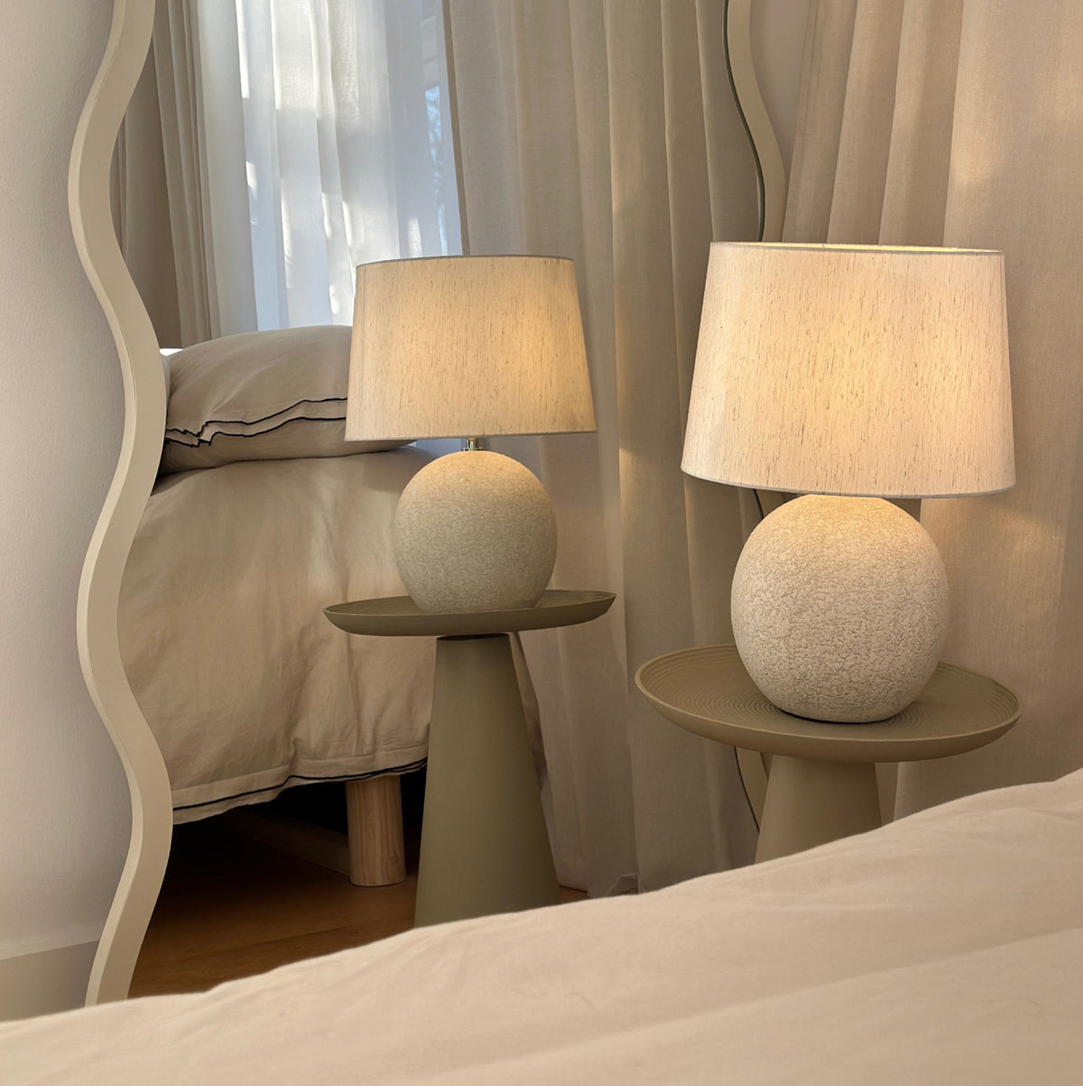Stone ceramic drum shade table lamp in irregular mirror reflecting warm lighting around room