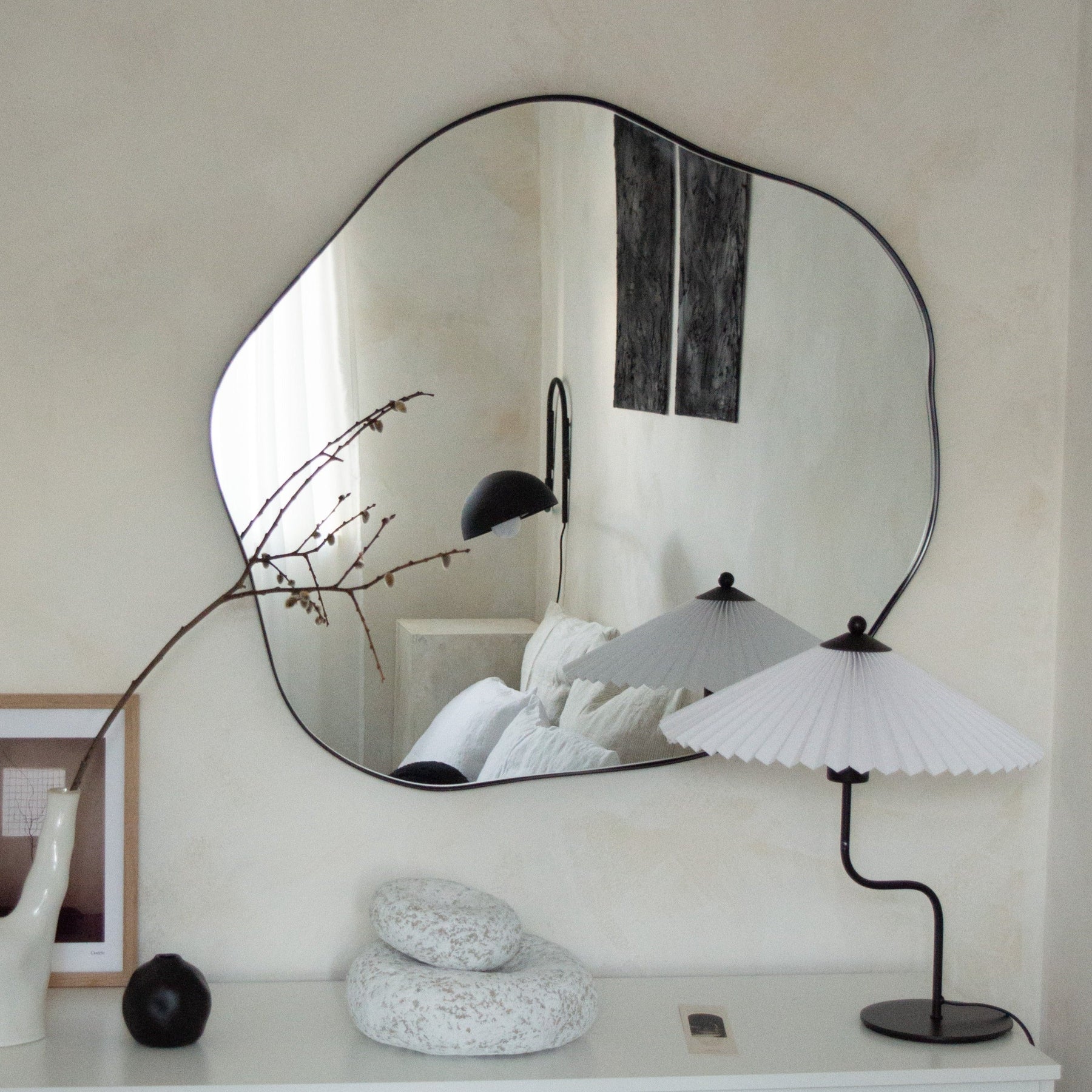 Black metal pond shaped irregular wall mirror displayed above console table