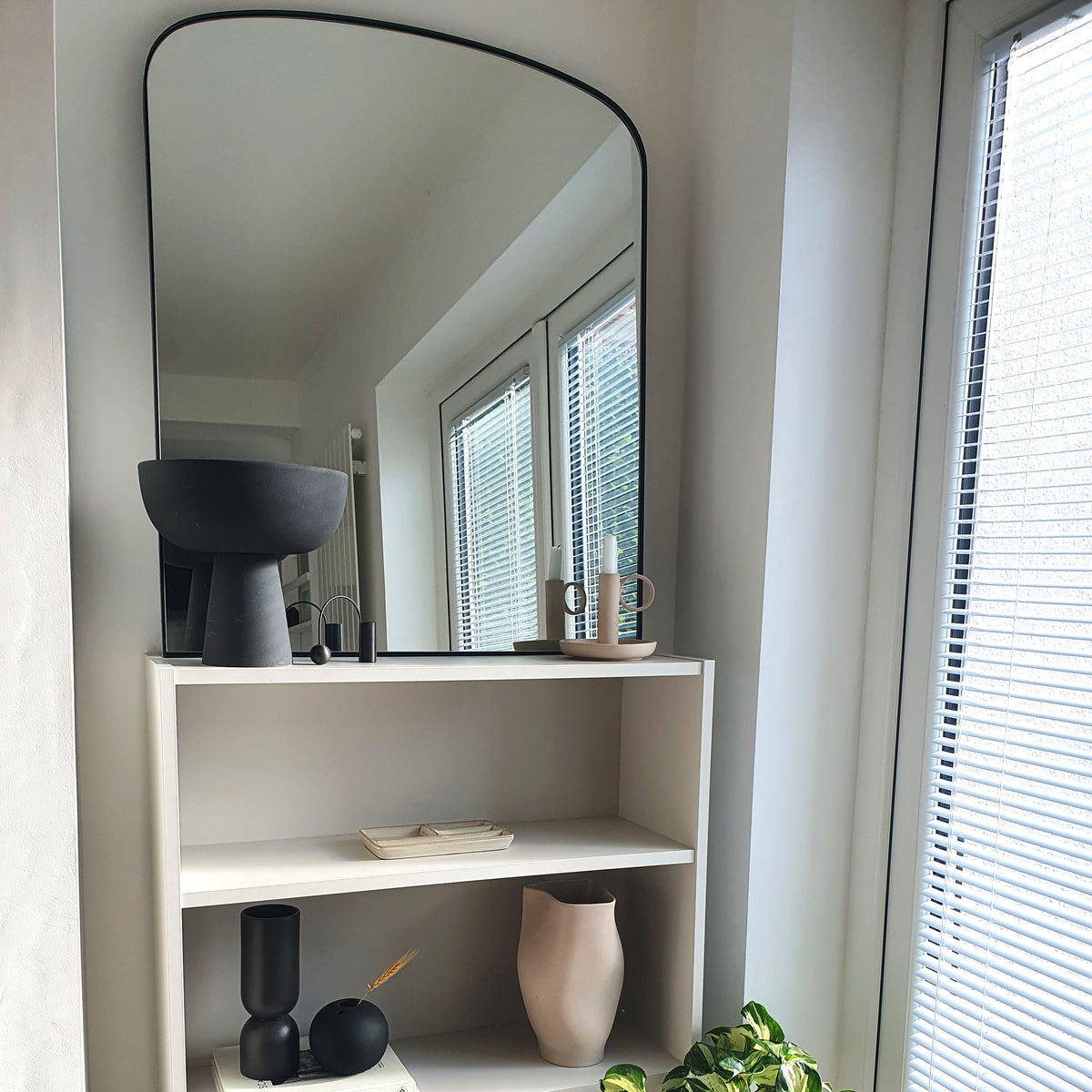 Black contemporary arched metal wall mirror displayed beside window