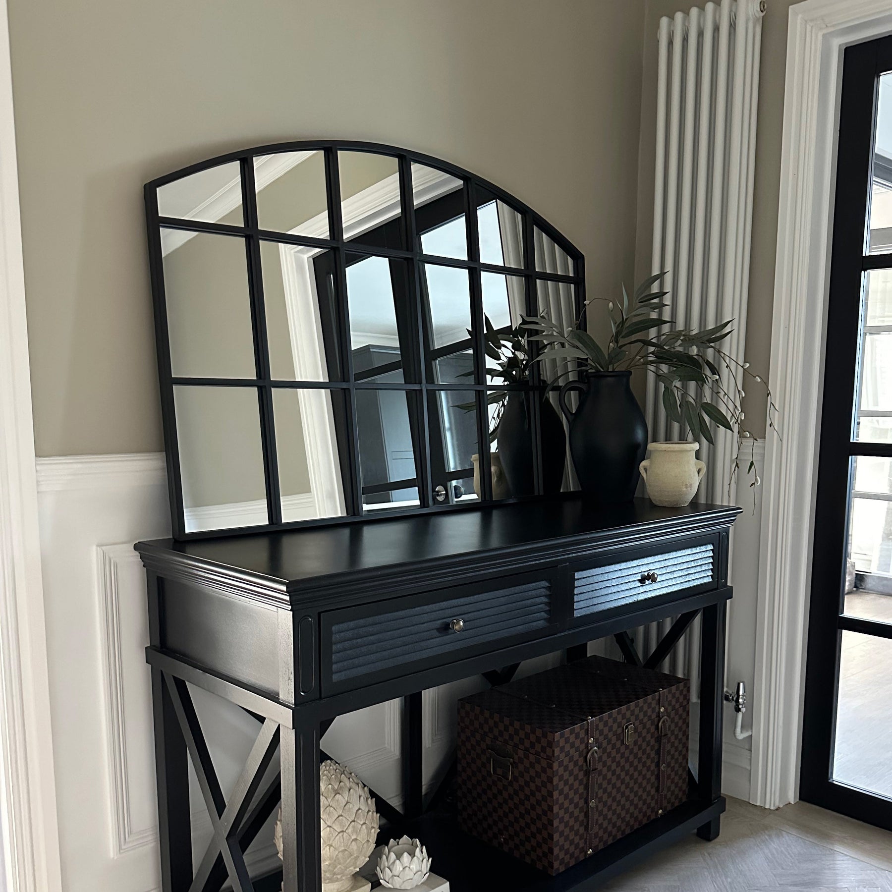 Black industrial arched metal window mirror displayed on console table