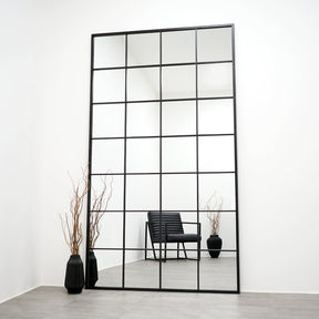 Full length extra large black industrial metal window mirror leaning against wall