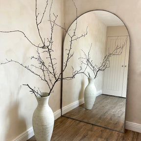 Champagne Full Length Arched Metal Mirror leaning against wall beside vase