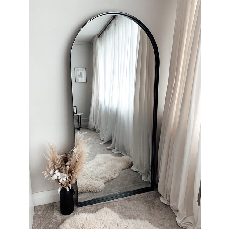 Full length arched black large metal mirror leaning against wall